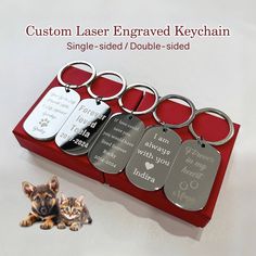 a set of six engraved keychains in a red box with a cat laying next to it