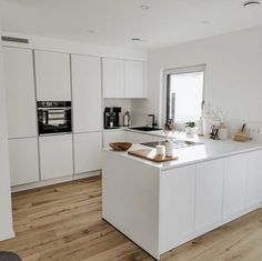 a kitchen with white cabinets and wood flooring next to an open doored window