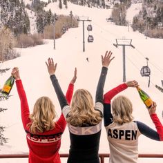 three women standing at the top of a ski lift with their arms in the air