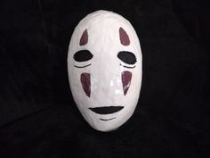 a white mask with red and black designs on it's face sitting on a black background