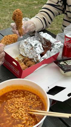 a bowl of ramen and some chicken nuggies on a picnic table with coca cola