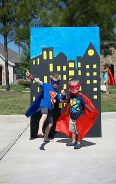 two young boys dressed up as superman and robin in front of a cityscape