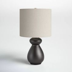 a black table lamp with a white shade on the base and a beige linen lampshade