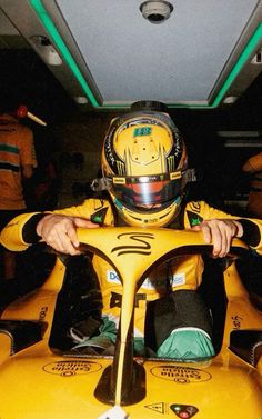 a man sitting in a yellow race car with his hands on the steering wheel and wearing a helmet