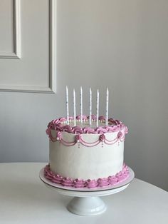 a white cake with pink icing and lit candles on it sitting on a table