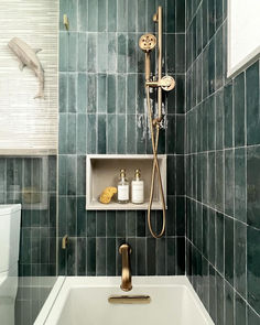 a bathroom with green tiles and gold fixtures in the bathtub, shower head, and shelf