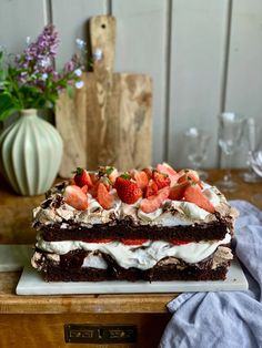 a cake with strawberries and cream on top sitting on a table next to a vase