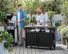 a man and woman cooking on an outdoor bbq grill in the back yard with potted plants