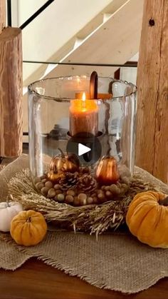 a table topped with a glass vase filled with pumpkins and other fall decorations on top of a wooden table