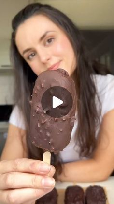 a woman holding a chocolate covered donut on a stick