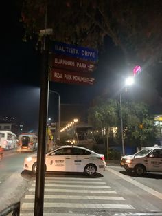 two cars are parked on the side of the road near a street sign at night