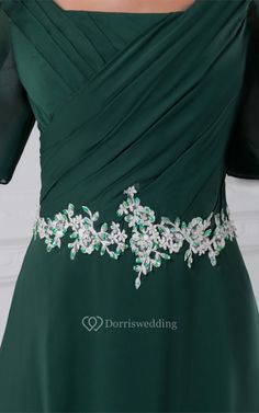 a woman wearing a green dress with white flowers on the waist and shoulder, in front of