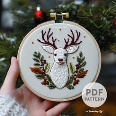 a hand holding a embroideryed deer ornament in front of a christmas tree