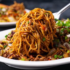 a white plate topped with spaghetti and meat next to another plate full of food on the table