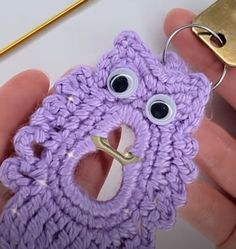 a purple crocheted phone case with eyes and a keychain attached to it