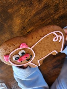 a person holding up a cookie shaped like a dog with pink ears and nose rings