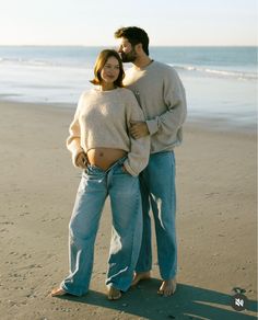 a pregnant woman and man standing on the beach with their belly wrapped around each other