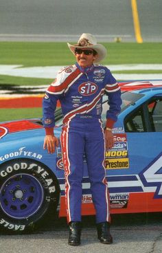 a man standing next to a racing car on a race track with his hat on