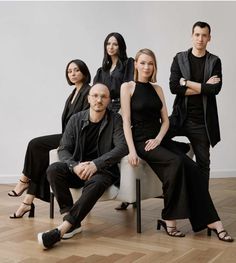 four people sitting on a chair in front of a white wall and hardwood flooring