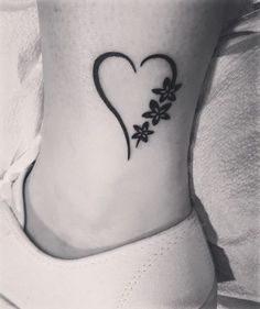 a black and white photo of a heart with flowers on the side of her ankle