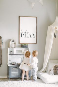 two children playing in a playroom with a poster on the wall above them that says let's play