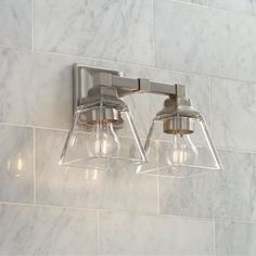 two light bathroom fixture with clear glass shades on the wall and white marble tile behind it