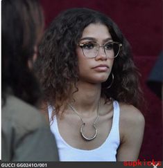 a close up of a person wearing glasses and a white tank top with long curly hair