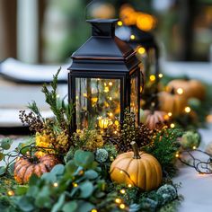 a lantern is lit up on the table with greenery and pumpkins