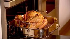 a turkey is being cooked in a roasting pan on an oven rack with the door open