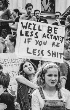 black and white photograph of people holding signs in front of a building that says we'll be less against if you are less shitt