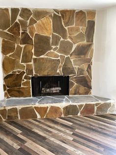 an empty room with a stone fireplace and hard wood flooring