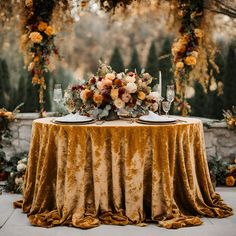 a table topped with a gold cloth covered tablecloth and flowers on top of it