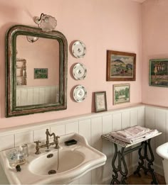 a bathroom with pink walls and pictures on the wall next to a pedestal sink in front of a mirror