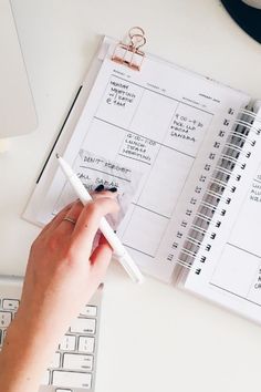 a person's hand is holding a pen over a planner