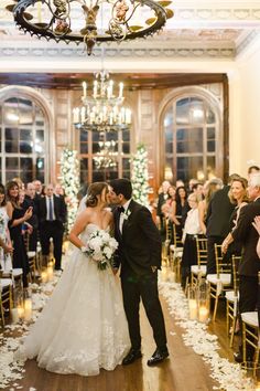 a bride and groom kiss as they walk down the aisle at their wedding ceremony in an elegant ballroom