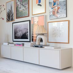 a white entertainment center with pictures on the wall above it and a lamp next to it