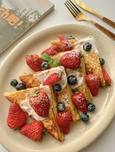 french toast with strawberries and blueberries on a white plate next to a book