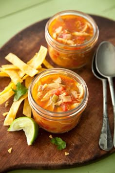 two jars filled with food sitting on top of a wooden cutting board next to silverware