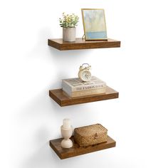 three wooden shelves with books and vases on them, one shelf has an alarm clock