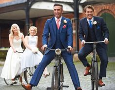 three men in suits and ties riding bicycles with one woman on the other side, smiling at the camera