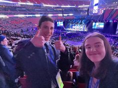 two people giving the thumbs up sign at a sporting event in an arena full of spectators