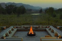 a fire pit surrounded by couches in the middle of an open field with mountains in the background