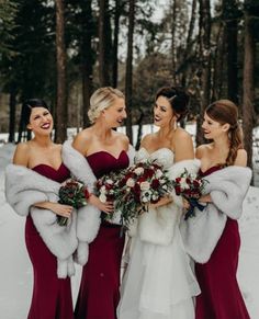 three bridesmaids in red dresses and fur stoles smile at each other while standing in the snow