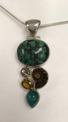 "Bold pendant in sterling silver featuring 5 different gemstones set in bezels and attached very closely together in a design.  A large oval piece of turquoise is at the top of the design.  The next \"row\" of stones are a round faceted quartz on the left and a snail shaped fossil on the right.  Beneath the quartz is a faceted opal shaped citrine and at the bottom of this design tower is a pear shaped turquoise with it's point towards the bottom.  The bezels are open in the back.  The bail at the top is very wide with a 10 mm wide opening.  The bail swings on a hinge. The pendant measures 2 3/4\" long by 1 1/16\" wide.  This pendant is preowned and in good condition. It can be purchased with or without the 18\" snake chain." Unique Multi-stone Turquoise Gemstones, Sterling Silver Multi-stone Jewelry With Oval Cabochon, Sterling Silver Oval Cabochon Multi-stone Jewelry, Sterling Silver Turquoise Necklace With Stones, Turquoise Multi-stone Gemstones In Sterling Silver, Sterling Silver Multi-stone Turquoise Necklace, Unique Oval Natural Gemstones, Statement Pendant, Multi Stone