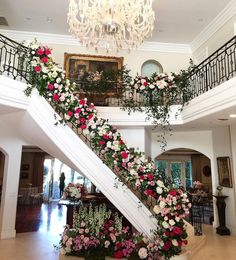 a staircase decorated with flowers and greenery in a large room next to a chandelier