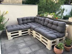 a couch made out of wooden pallets sitting on top of a cement floor next to potted plants