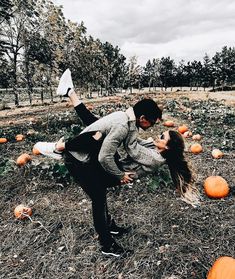 a man and woman dancing in a field full of pumpkins with one holding the other's leg