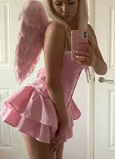 a woman in a pink dress taking a selfie with her cell phone while wearing an angel costume