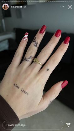 a woman's hand with red fingernails and tattoos on her left thumb, showing the ring finger tattoo