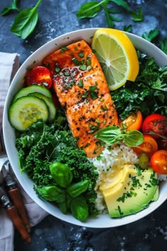 a white bowl filled with salmon, rice, vegetables and sliced lemons on top of a blue surface